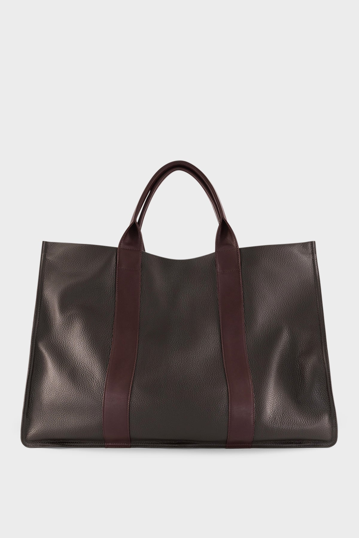 An extra-large dark brown tote bag with a rectangular body. It has a wide top with two magnetic closures. The bag has 2 handles to be carried handheld or as a shoulder bag.