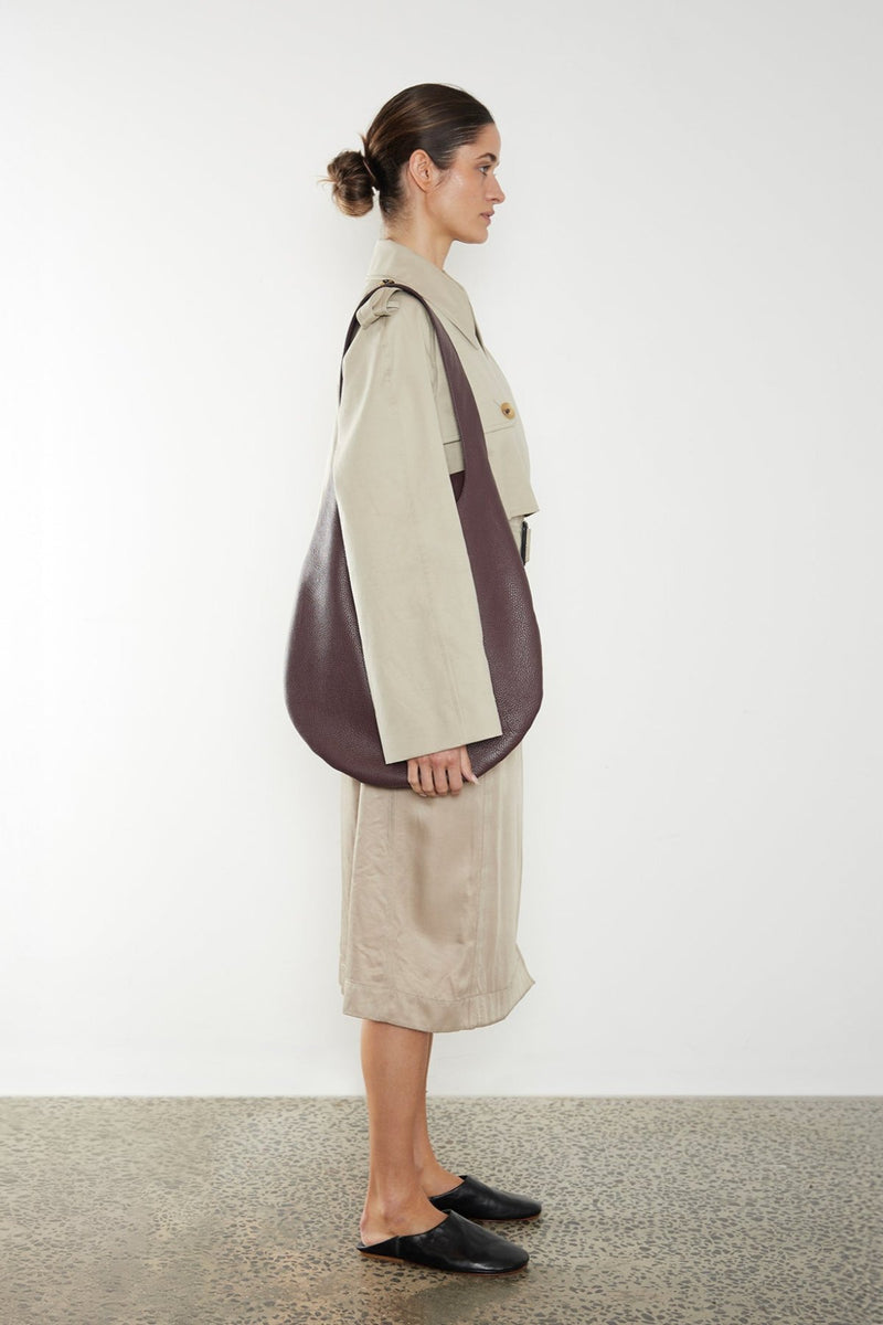 A woman carrying the One Hobo shoulder bag. It shows a front angle of the hobo showcasing its soft slouch in the bag's body. It can carry everyday essentials and can be used as a work bag or a travel bag.