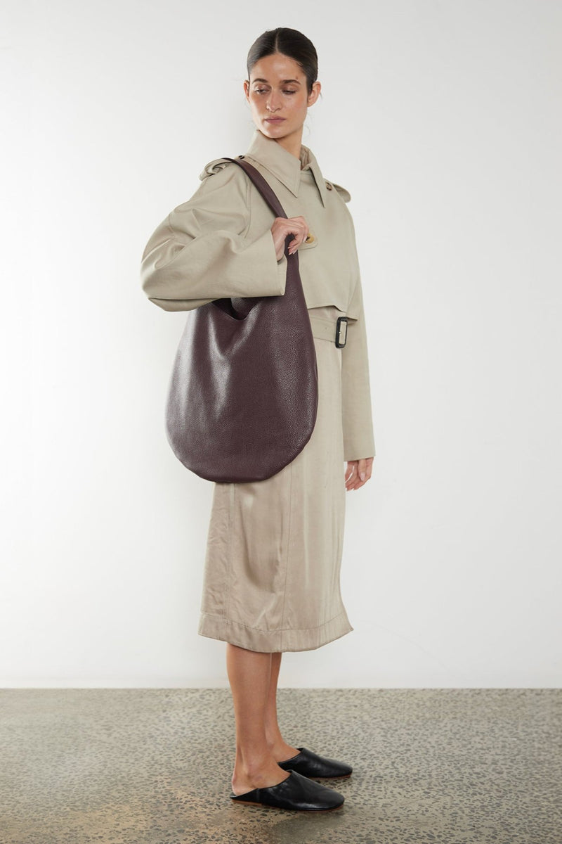 A woman carrying the One Hobo shoulder bag. It shows a side angle of the hobo showcasing its slim body. It can carry everyday essentials and can be used as a work bag or a travel bag.