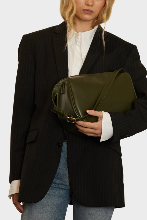 A woman carrying the saddle shoulder bag in her arms for size reference. The handbag is medium-sized with a structured body.