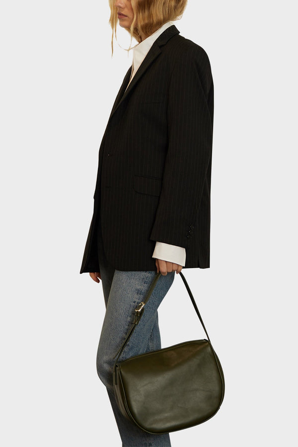 A woman holding the shoulder bag on its strap. The bag has a soft slouch and spacious body with fine stitching.