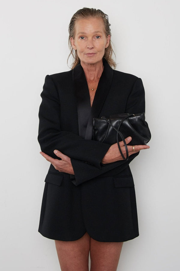 A woman carrying the black mini clutch bag with its removable strap hanging. This handbag can be used both as a shoulder bag or a purse clutch.