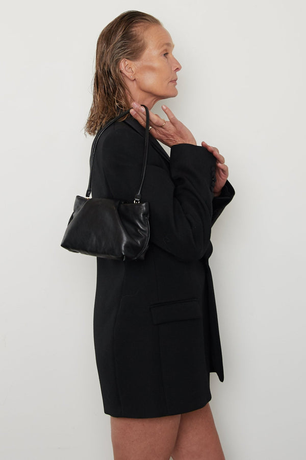 A woman carrying the mini fold clutch bag with its handles up to function as a shoulder bag. The mini bag features a modern and structured design.