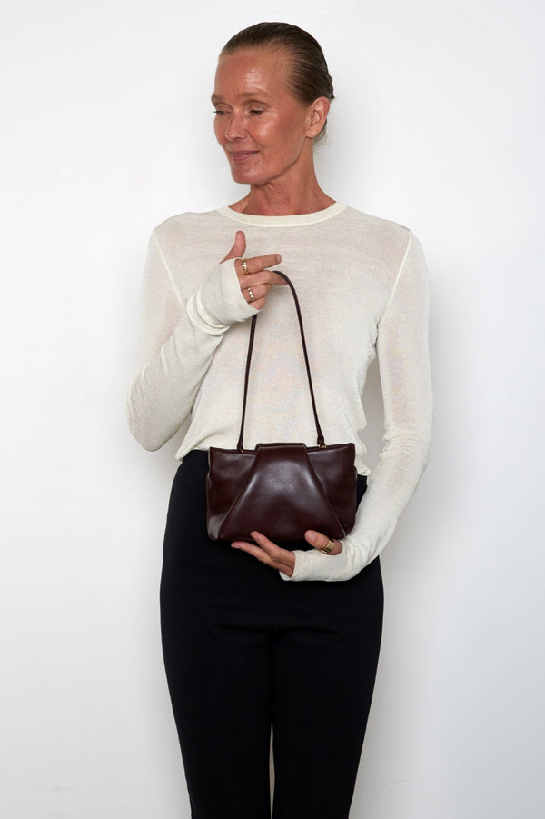 A woman carrying the mini fold clutch bag with its handles up to function as a shoulder bag. The mini bag features a modern and structured design.