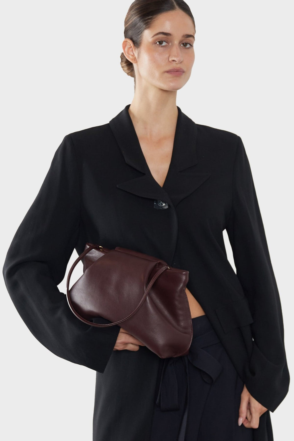 A woman carrying the burgundy fold clutch bag handheld. The bag can carry enough daily essentials and is suited for both work and party.