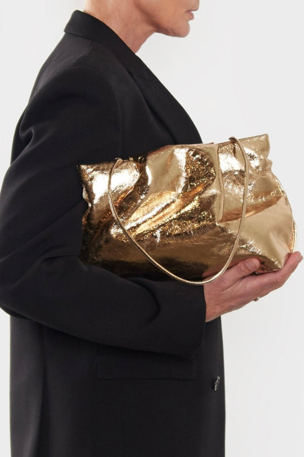 A woman carrying the gold fold clutch bag handheld. The bag can carry enough daily essentials and is suited for both work and party.