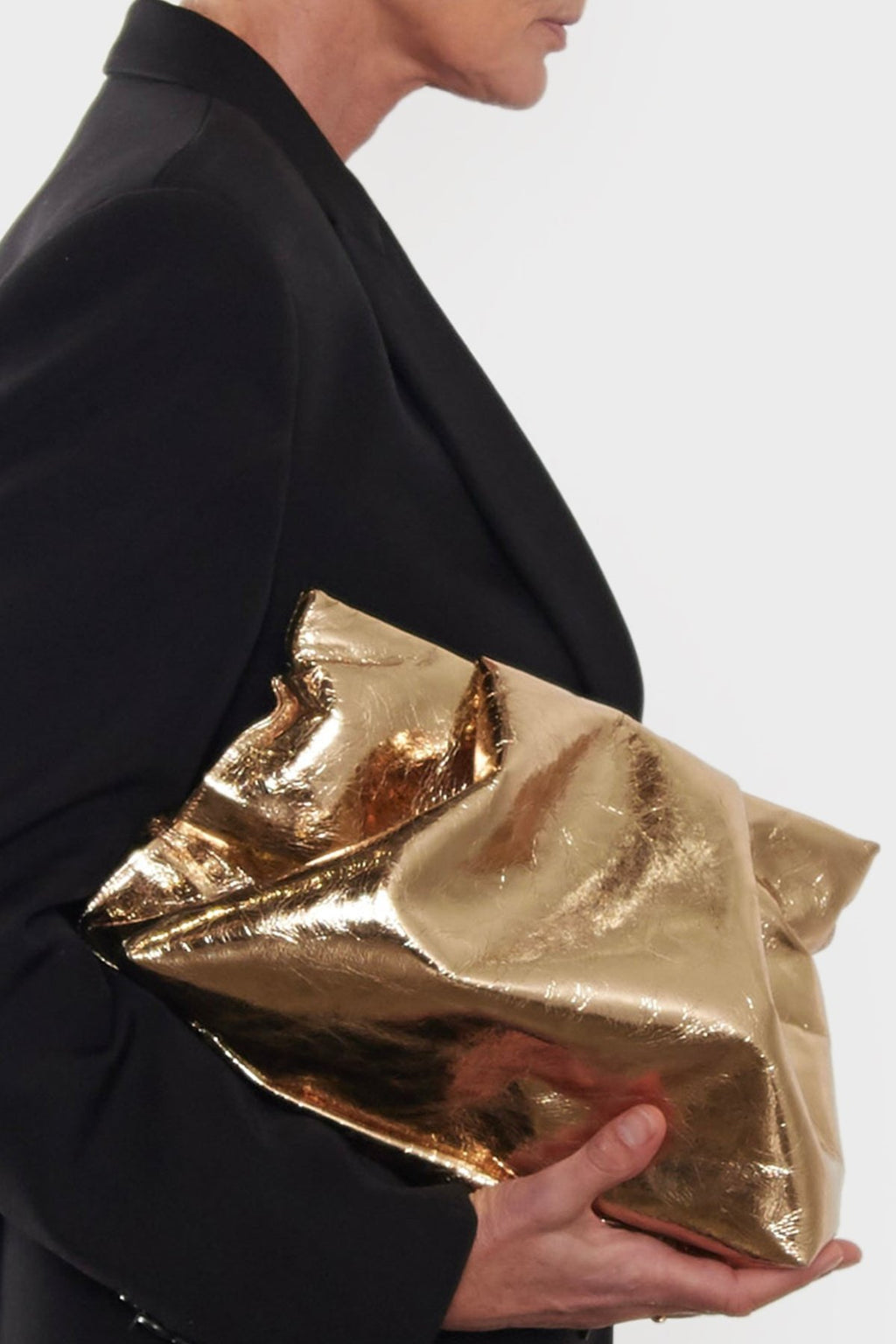 A side angle of the gold Fold clutch bag. The handbag has a modern design suited as a work bag or a clutch purse for events.