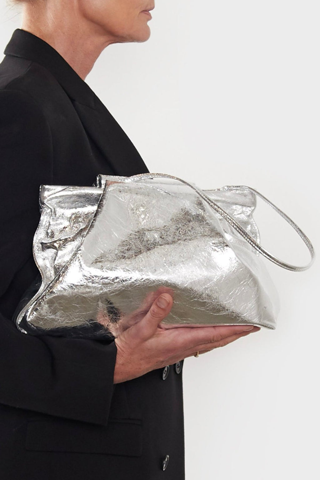 A side angle of the silver Fold clutch bag. The handbag has a modern design suited as a work bag or a clutch purse for events.