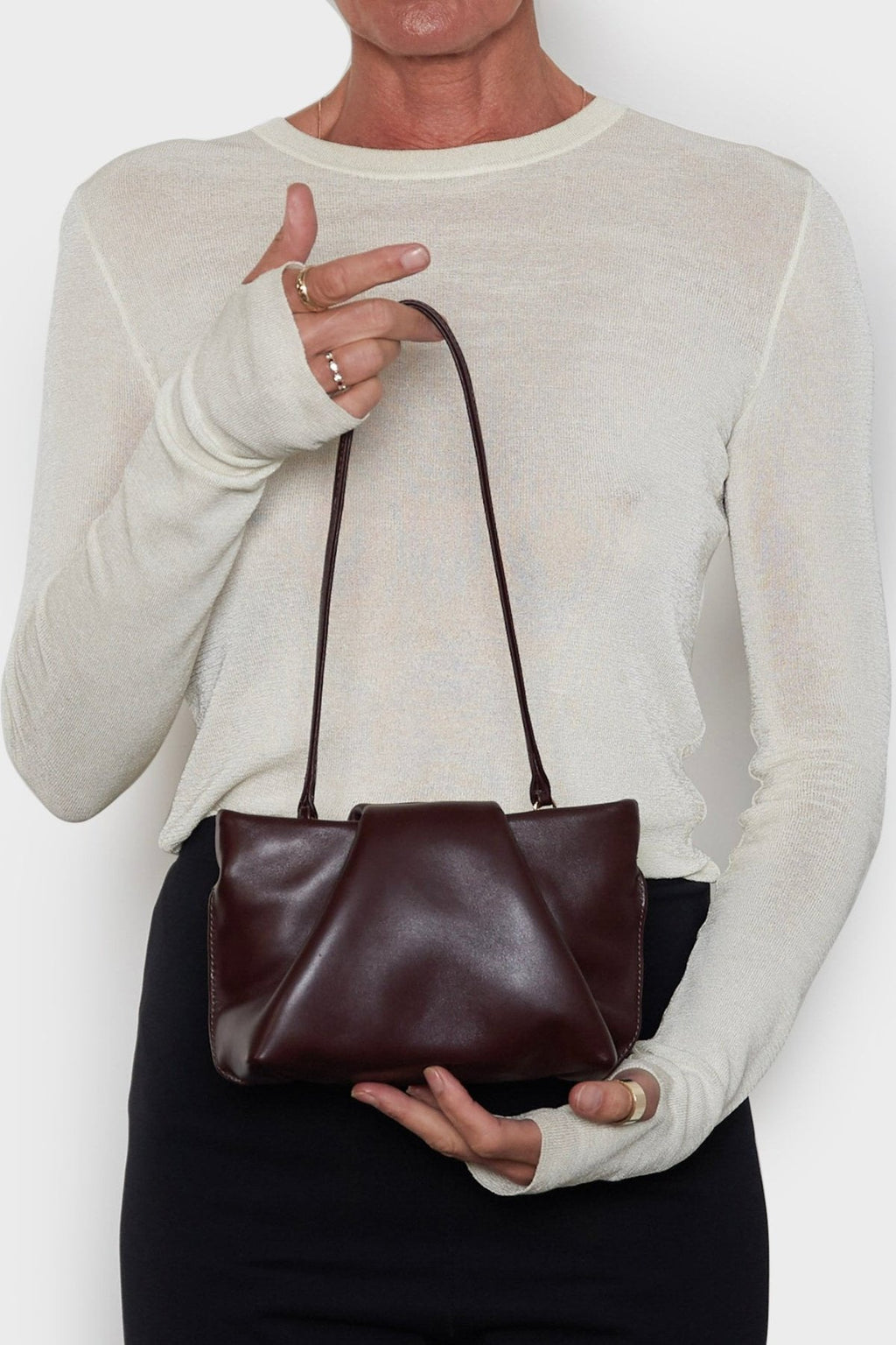 A woman carrying the mini fold clutch bag with its handles up to function as a shoulder bag. The mini bag features a modern and structured design.