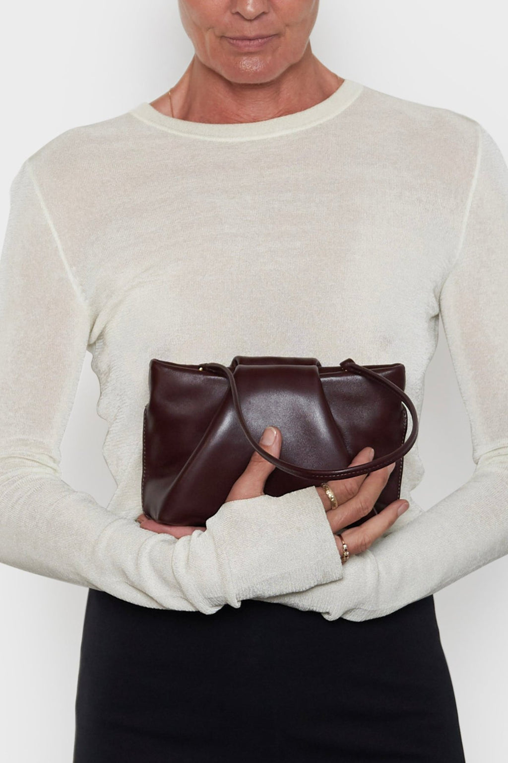 A woman carrying the burgundy mini clutch bag handheld. This handbag is suited as a purse clutch for events.