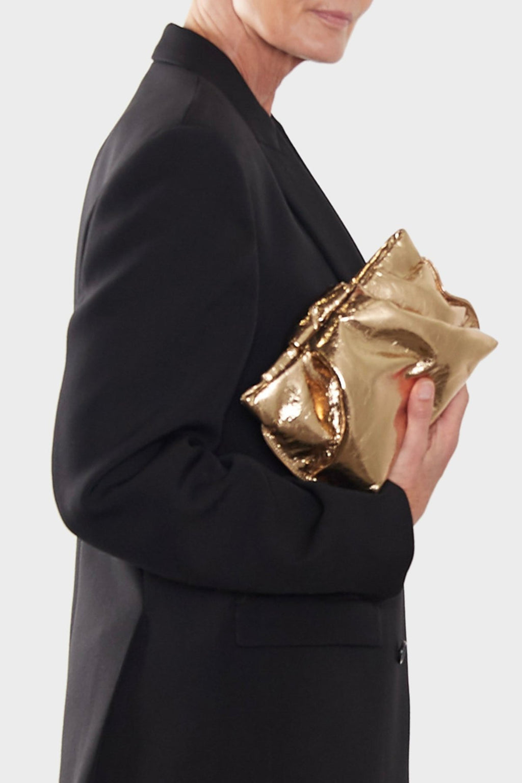 A woman carrying the gold mini clutch bag handheld. This handbag is suited as a purse clutch for events.