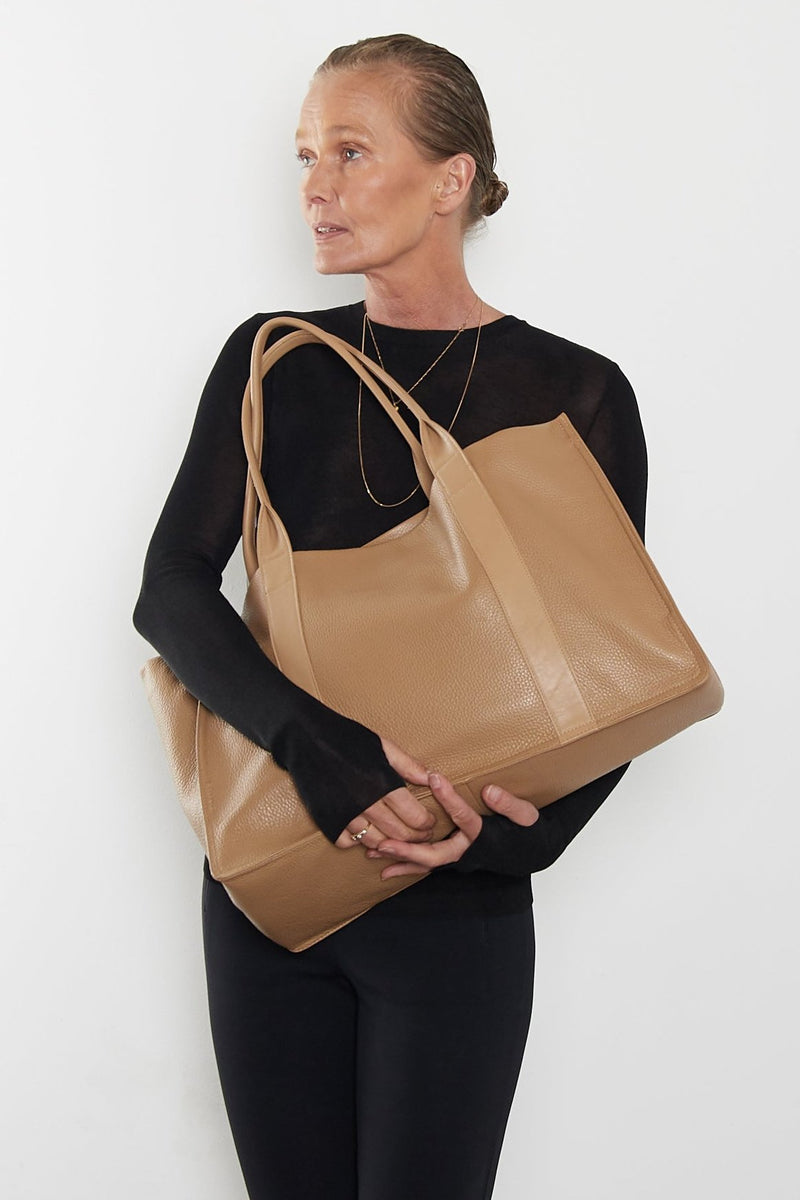 An image of a woman carrying the Grocer tote bag in her arms. The bag can be used as a work bag or a travel bag. 