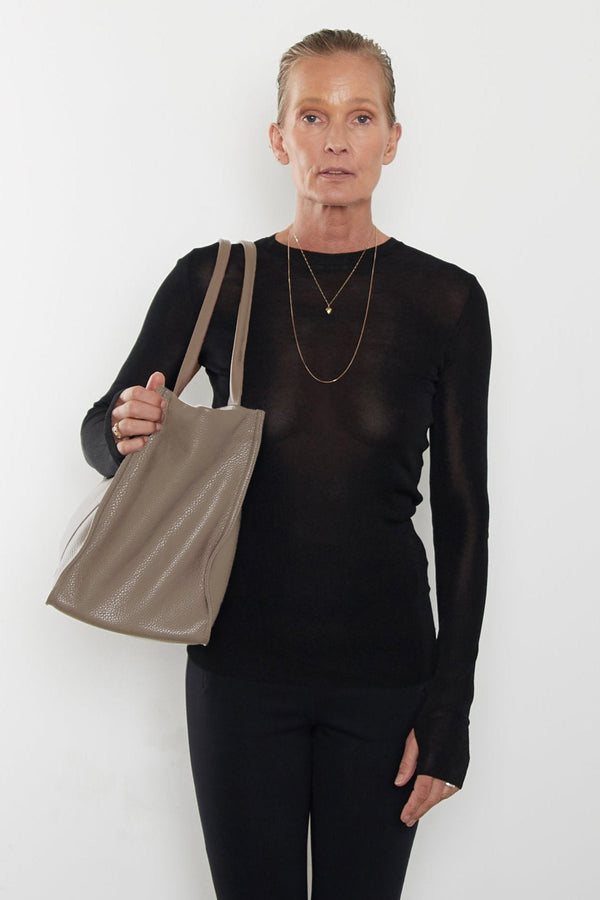 An image of a woman carrying the Grocer tote bag in her arms. The bag can be used as a work bag or a travel bag.