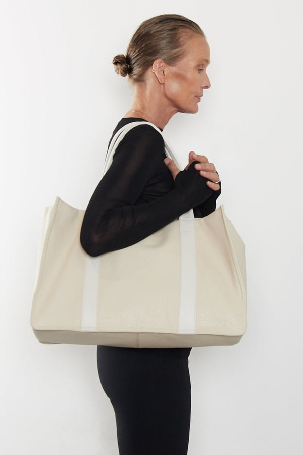 An image of a woman wearing the Grocer tote as a shoulder bag. It features the front of the bag with its wide structured body.