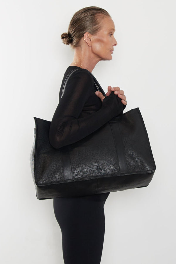 An image of a woman wearing the Grocer tote as a shoulder bag. It features the front of the bag with its wide structured body.