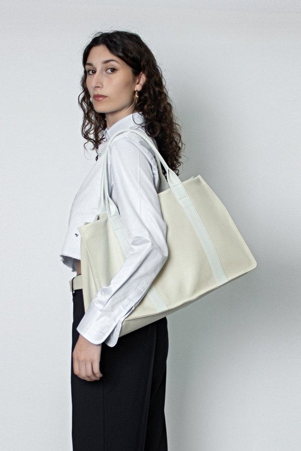 A woman carrying the Grocer tote bag in her arms. The bag can be used as a work bag or a travel bag. 