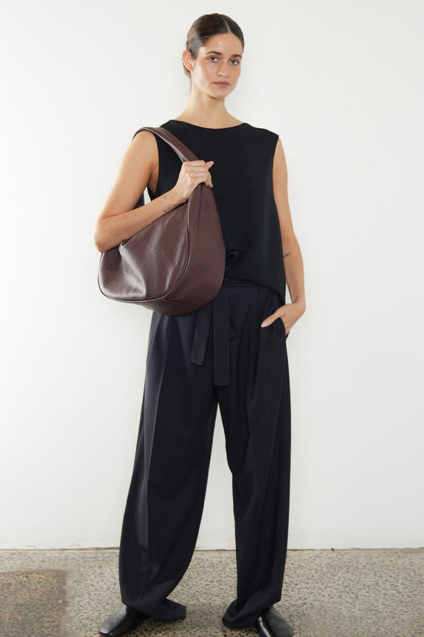 A woman carrying the halo shoulder bag. It shows a side angle of the satchel showcasing its large structured body. It can carry everyday essentials and can be used as a work bag or a travel bag.
