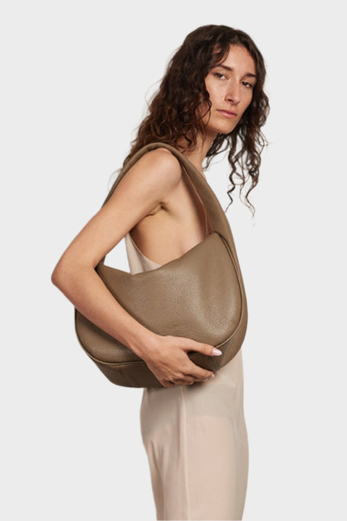 A woman wearing the halo day shoulder bag. It shows the front of the bag with its fine hand stitching and hobo inspired design.