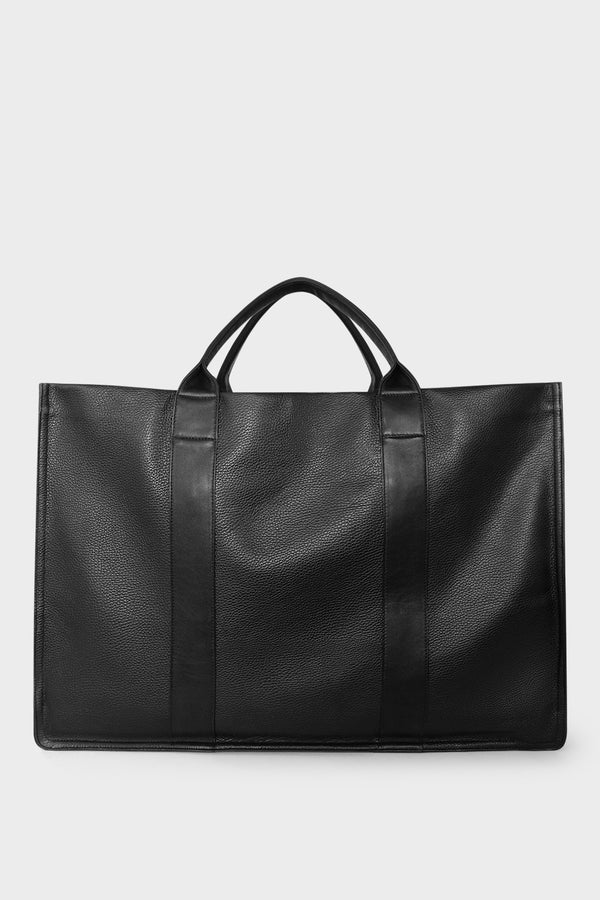 An extra-large black tote bag with a rectangular body. It has a wide top with two magnetic closures. The bag has 2 handles to be carried handheld or as a shoulder bag.