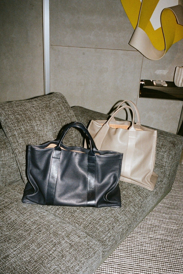 A lifestyle image of Grocer Tote Bags in Black and Grey laid on the couch.