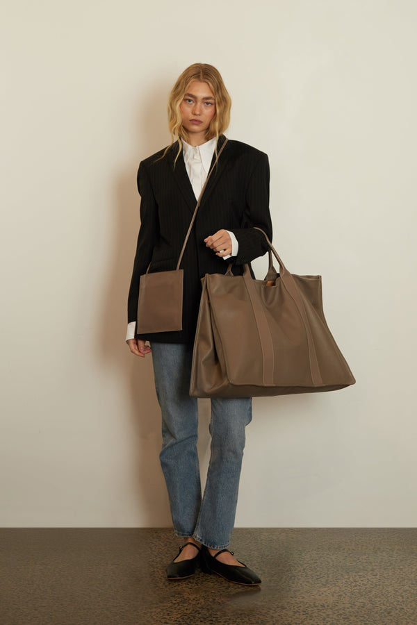 A woman carrying the Jumbo Grocer Tote in the crook of her arms. The bag suits as a weekender carry all travel bag.