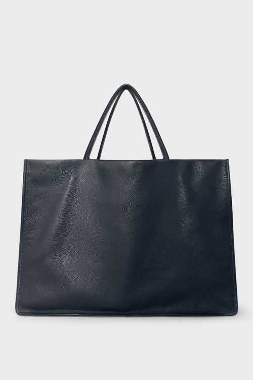 An extra-large navy blue tote bag with a square body. It has an open top with two magnetic closures. The bag has 2 handles to be carried handheld or as a shoulder bag.