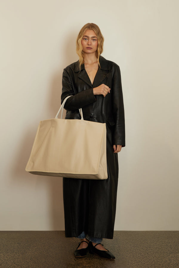 An image of a woman carrying the Jumbo Suite Tote Bag on the crook of her arm. With two handles, the tote can be carried handheld or as a shoulder bag.