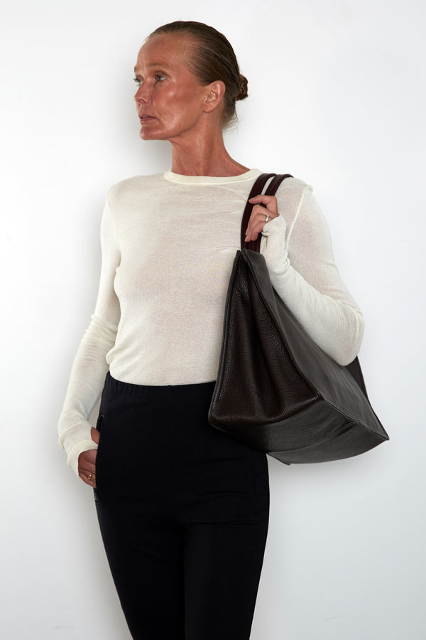 An image of a woman wearing the Junior Suite tote as a shoulder bag. It features the front of the bag with its wide structured body suited as a work bag.