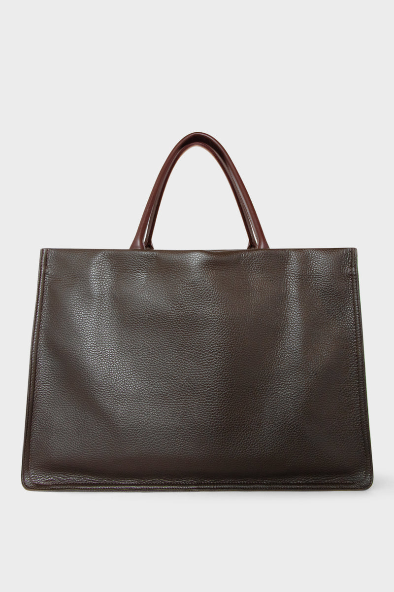 A large dark brown tote bag with a rectangular body. It has a wide top with a magnetic closure. The bag has 2 handles to be carried handheld or as a shoulder bag.