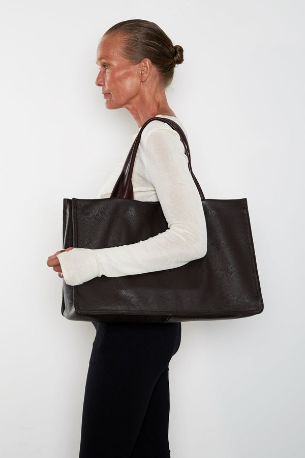 An image of a woman wearing the Junior Suite tote as a shoulder bag. It features the front of the bag with its wide structured body.