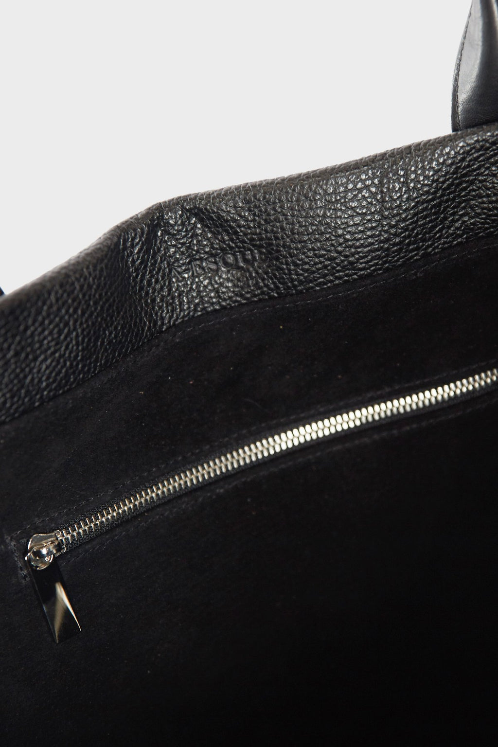 The photo shows the interior of the tote bag. It has 1 zipperd pocket in silver hardware. The interior is lined with a black suede leather. This shoulder bag  is called Large Grocer Leather Tote