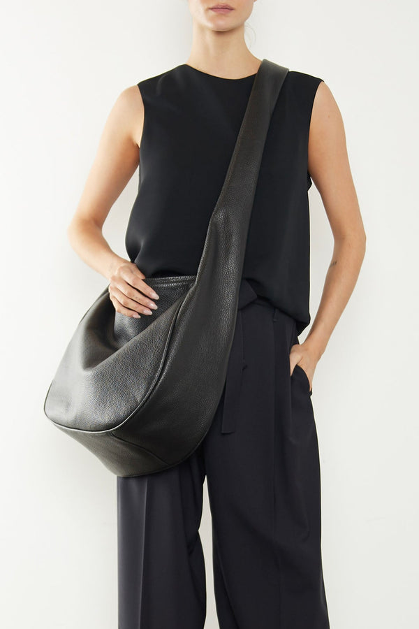 A woman wearing the Large Halo crossbody bag slung across her body. It shows a side angle of the satchel highlighting its large and structured body. It can carry everyday essentials and can be used as a work bag or a cary all travel bag.