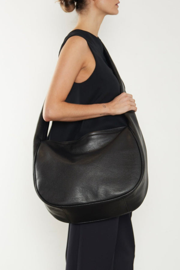 A woman wearing a crossbody bag slung across her body. It shows a front angle of the satchel showcasing its large structured body. It can carry everyday essentials and can be used as a work bag or a travel bag.