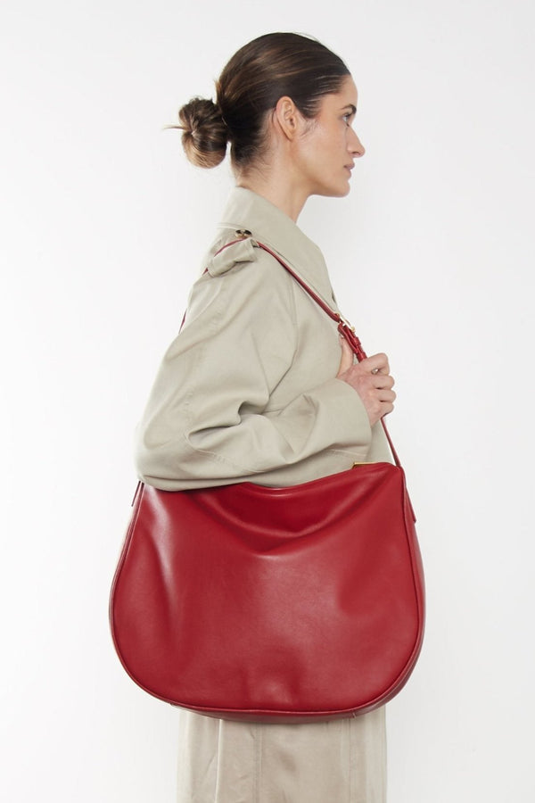 A woman carrying the Saddle red shoulder bag. It shows the front angle of the bag with its large body suited as a travel bag.