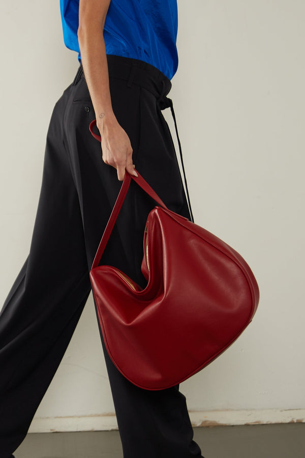 A woman carrying the red large saddle shoulder bag handheld through its handles. 