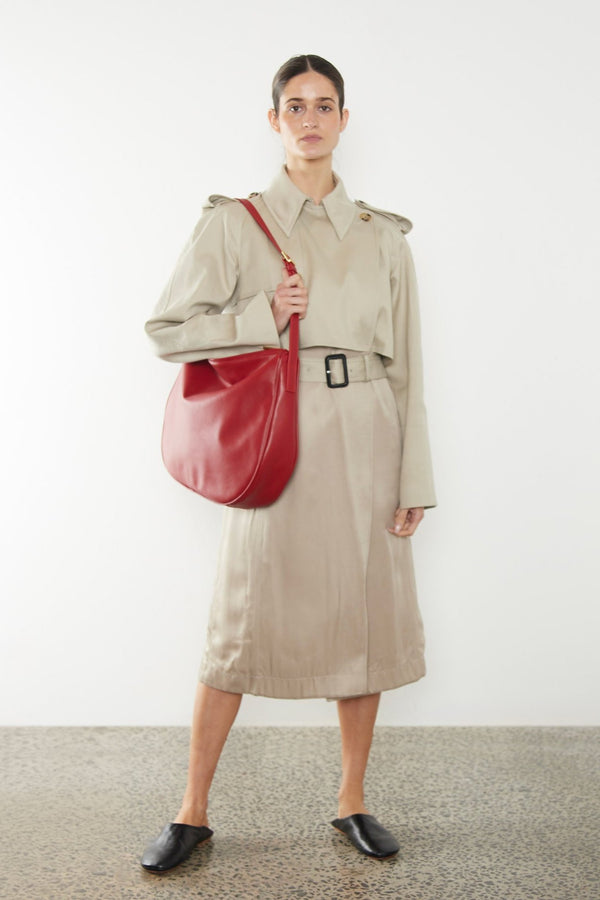 A woman wearing the large red saddle shouder bag. It shows a side angle of the satchel showcasing its large but slim body. It can carry everyday essentials and can be used as a work bag or a travel bag.