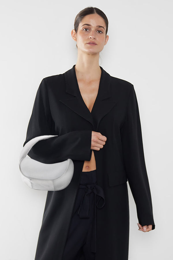 A woman carrying the Halo Mini bag in the crook of her arm. It shows the front angle of the handbag with its petite structured body. 