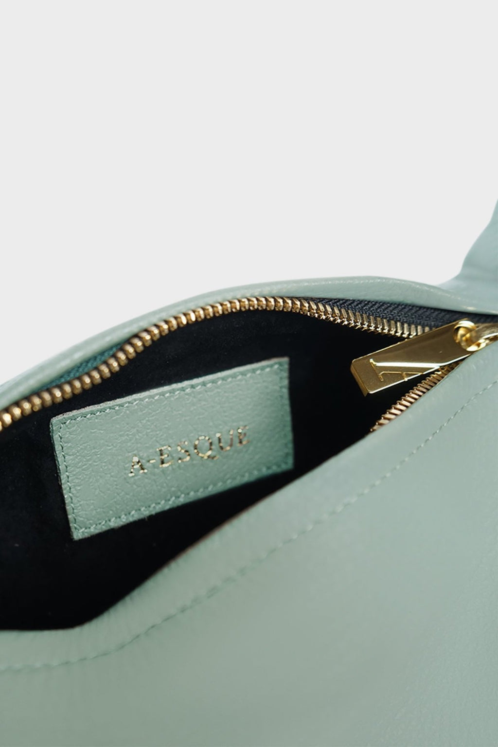 The mini halo bag has a black suede interior lining with an A-esque tag sewn inside. The shoulder bag features a gold hardware zipper. This small clutch purse is called Mini Halo Bag in Smooth Mint.