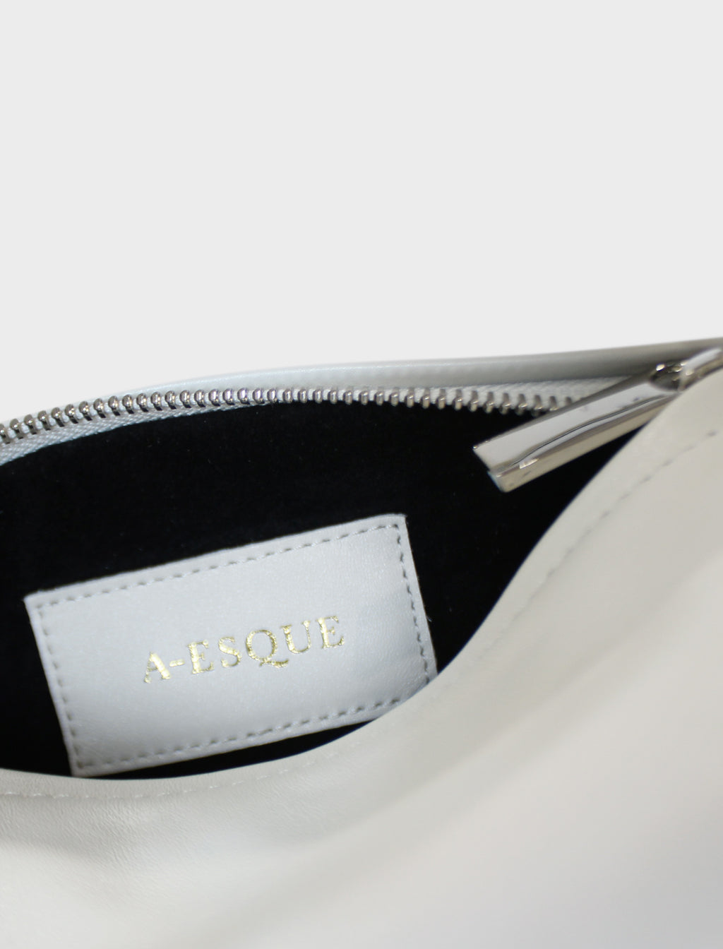 The mini halo bag has a black suede interior lining with an A-esque tag sewn inside. The shoulder bag features a silver hardware zipper. This small clutch purse is called Mini Halo Bag in Smooth Off White.