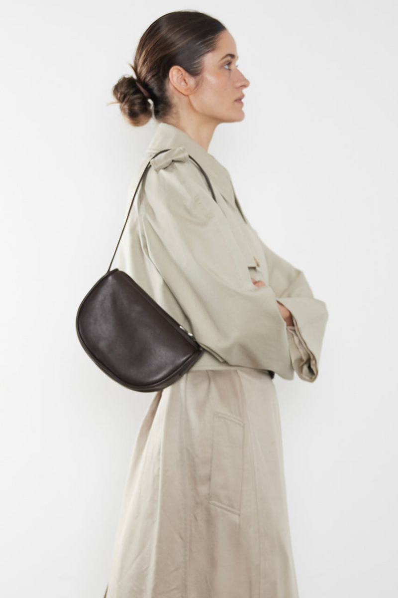 A woman wearing a small shoulder bag. It shows the front angle of the bag and its small compact body.