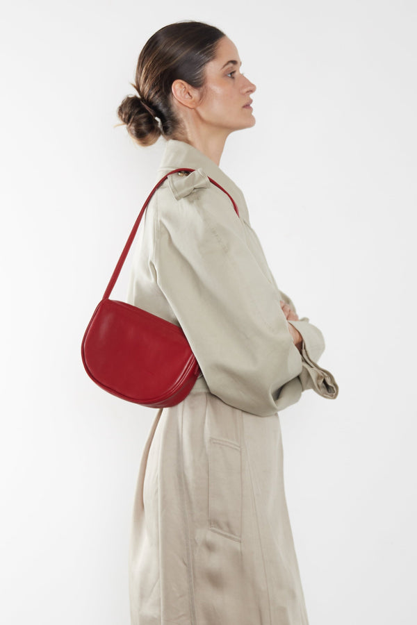 A woman wearing a small shoulder bag. It shows the front angle of the bag and its slim compact body.