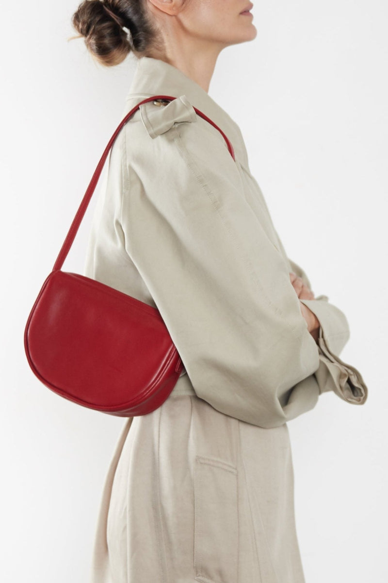 A woman wearing a small shoulder bag. It shows the front angle of the bag and its slim compact body.