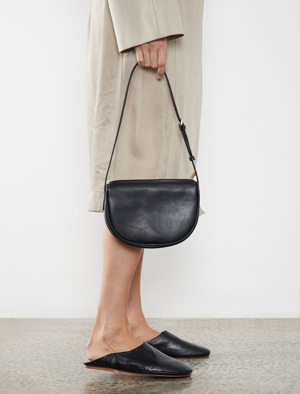 The mini saddle shoulder bag in black is carried handheld through its strap. With a soft slouch and slim silhouette, this small shoulder bag can carry everyday essentials like sunglasses, car keys, wallet, and lipstick.