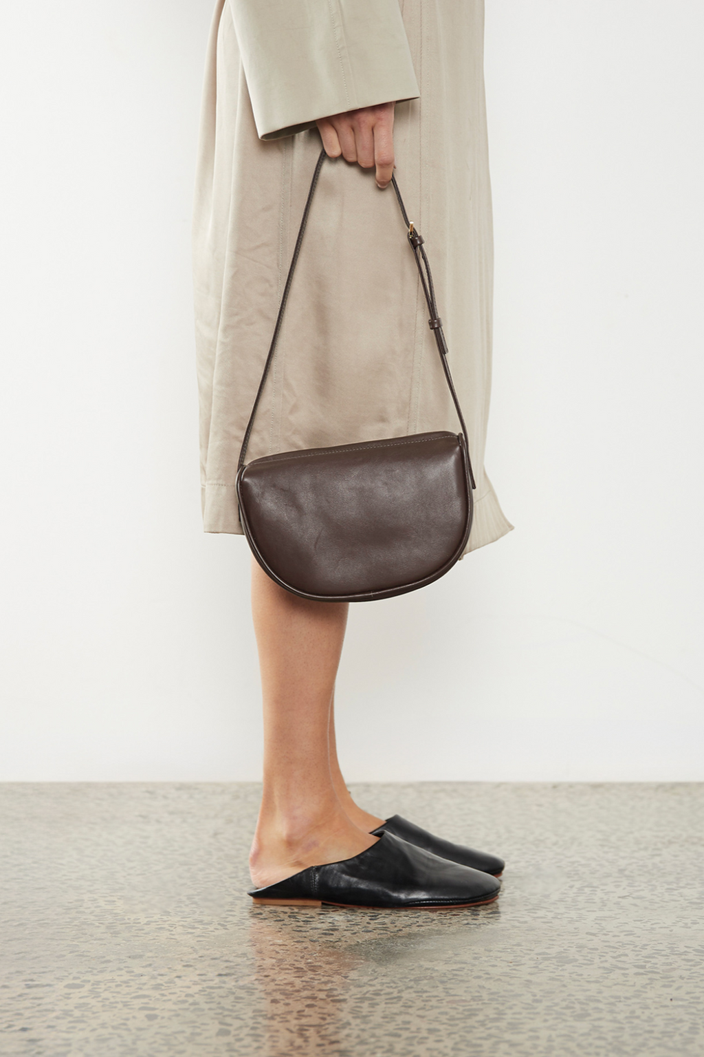 The mini saddle shoulder bag in dark brown is carried handheld from its strap. This small bag has a saddle inspired design showing a slim silhouette. It is suited as a casual bag for parties and as an everyday small shoulder bag.