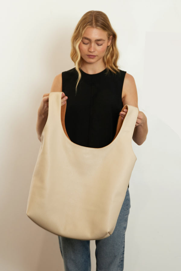 A woman holding the reversible sack tote through its handles.