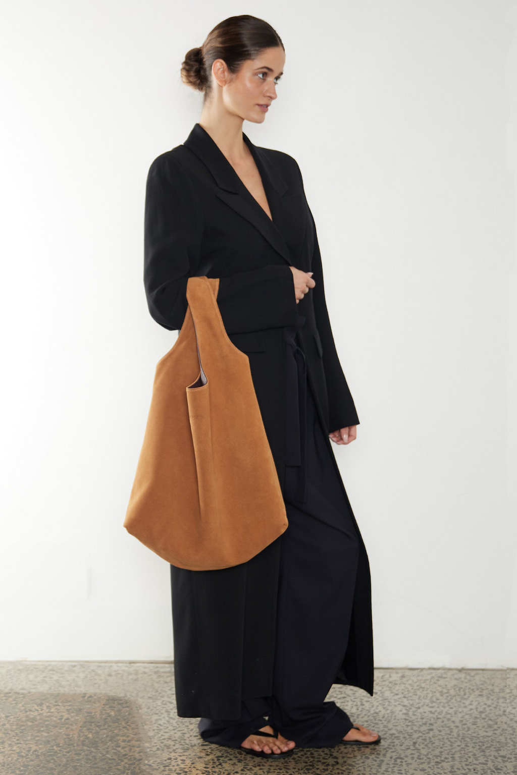 The reversible sack tote bag has two sides. The image shows the suede brown side of the tote carried on the crook of the arm.