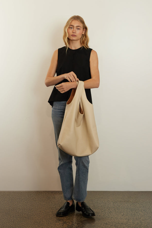 A woman carrying the tote bag in the crook of her arm. The bag can be carried handheld and is suited as a travel bag.