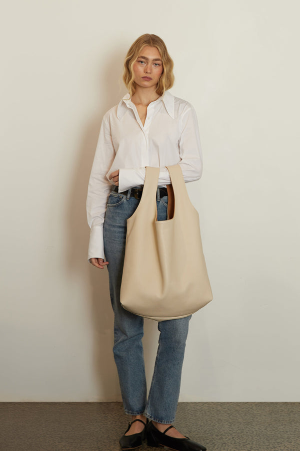 A woman carrying the white tote bag in the crook of her arm. The bag can be carried handheld or as a shoulder bag.