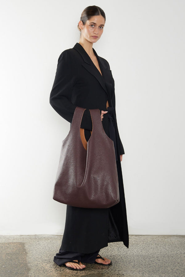 A woman carrying the Reversible Tote Bag slung in the crook of the arm. This burgundy tote bag suits as an everyday large shoulder bag but also stylish to be a travel bag or a beach bag.