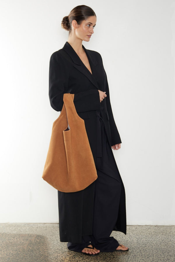 A woman carrying the Reversible Tote Bag in its Tan Suede side. The bag slung in the crook of the arm and suits as an everyday large tote bag but also stylish to be a travel bag or a beach bag.